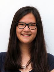 Profilbild von Emilie Scheer. Sie hat dunkle lange offene Haare und Trägt eine Brille. Sie steht vor einem weißen Hintergrund und lächelt breit.