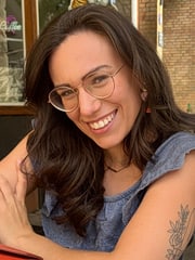 Amanda hat lange braune Haare und trägt eine Brille. Sie lächelt breit in die Kamera.