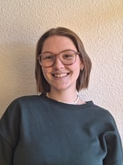 Antonia hat kinnlange Haare und trägt eine Brille. Sie lächelt in die Kamera.